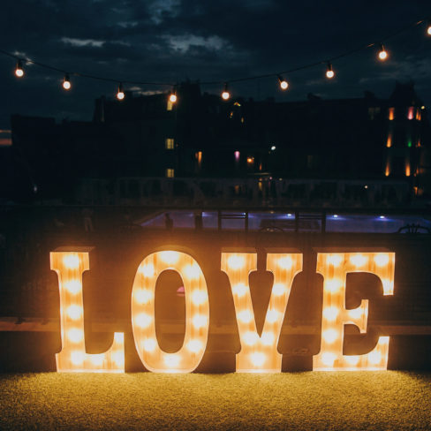 big white love letters in light bulbs for photo booth at wedding reception in night outdoors. love word lights, stylish evening decor for wedding ceremony